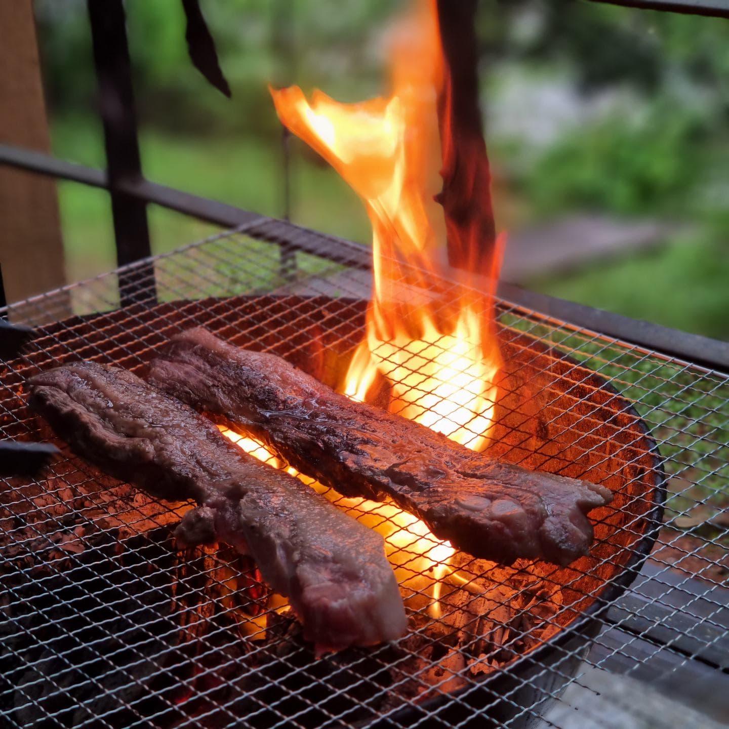 Meat searing over open flames on a charcoal grill