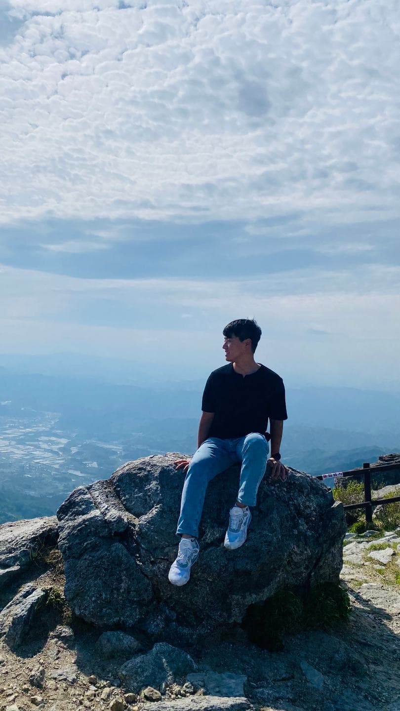 Sitting on the summit rocks with the hazy ranges behind