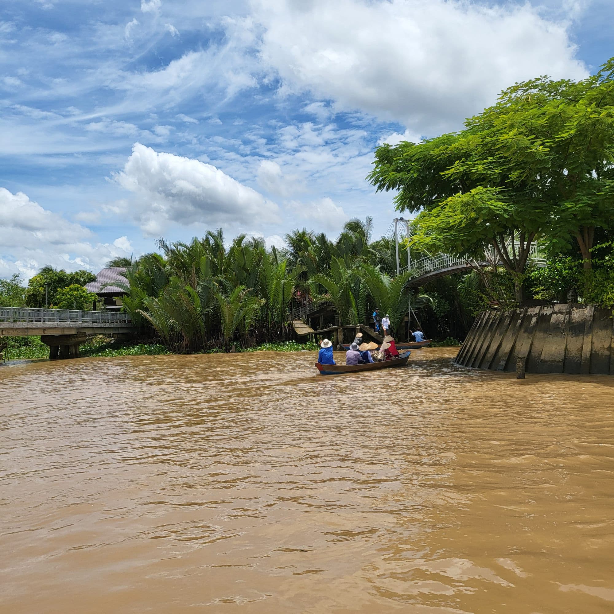 A small boat on the wide brown river, palms along the bank