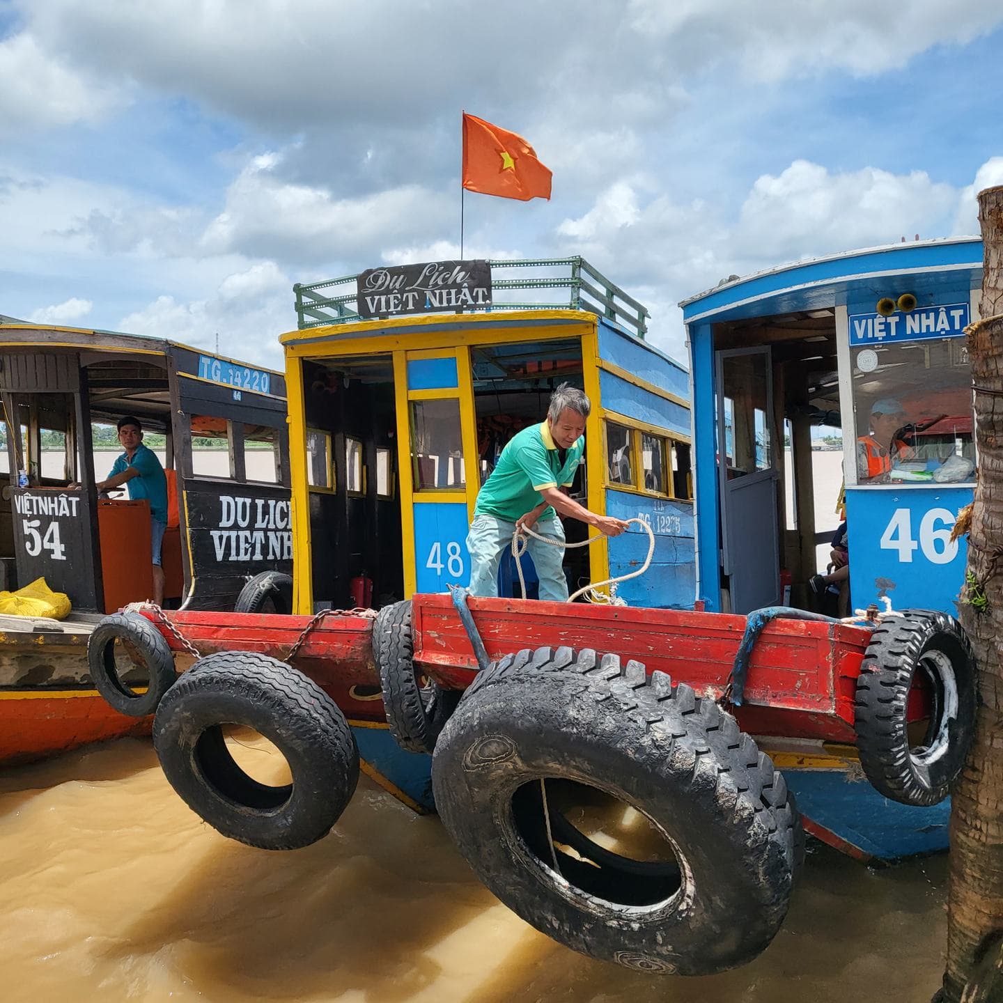 Tour boats moored with tyre fenders, a Vietnamese flag above