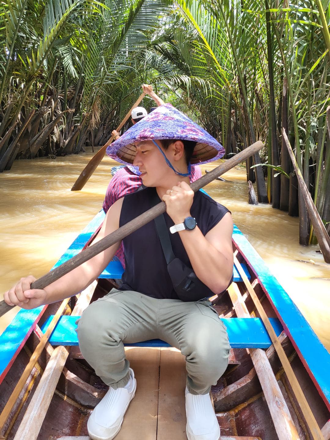 In a narrow boat among water palms, wearing a conical hat and holding an oar
