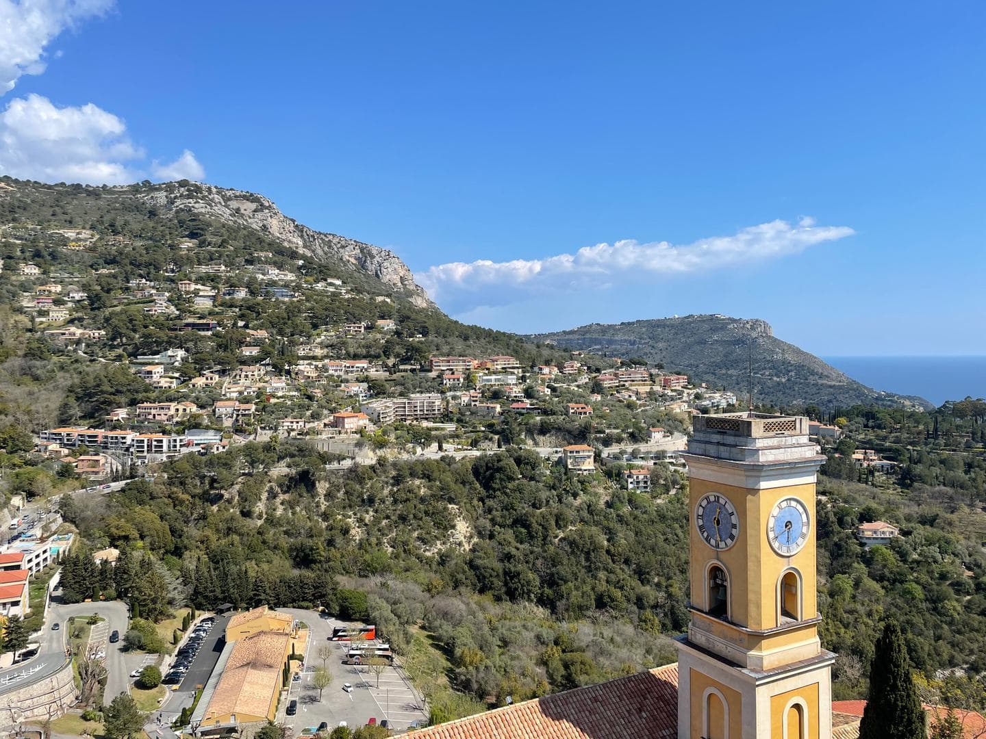 The yellow bell tower of Èze’s church with hills and villas behind