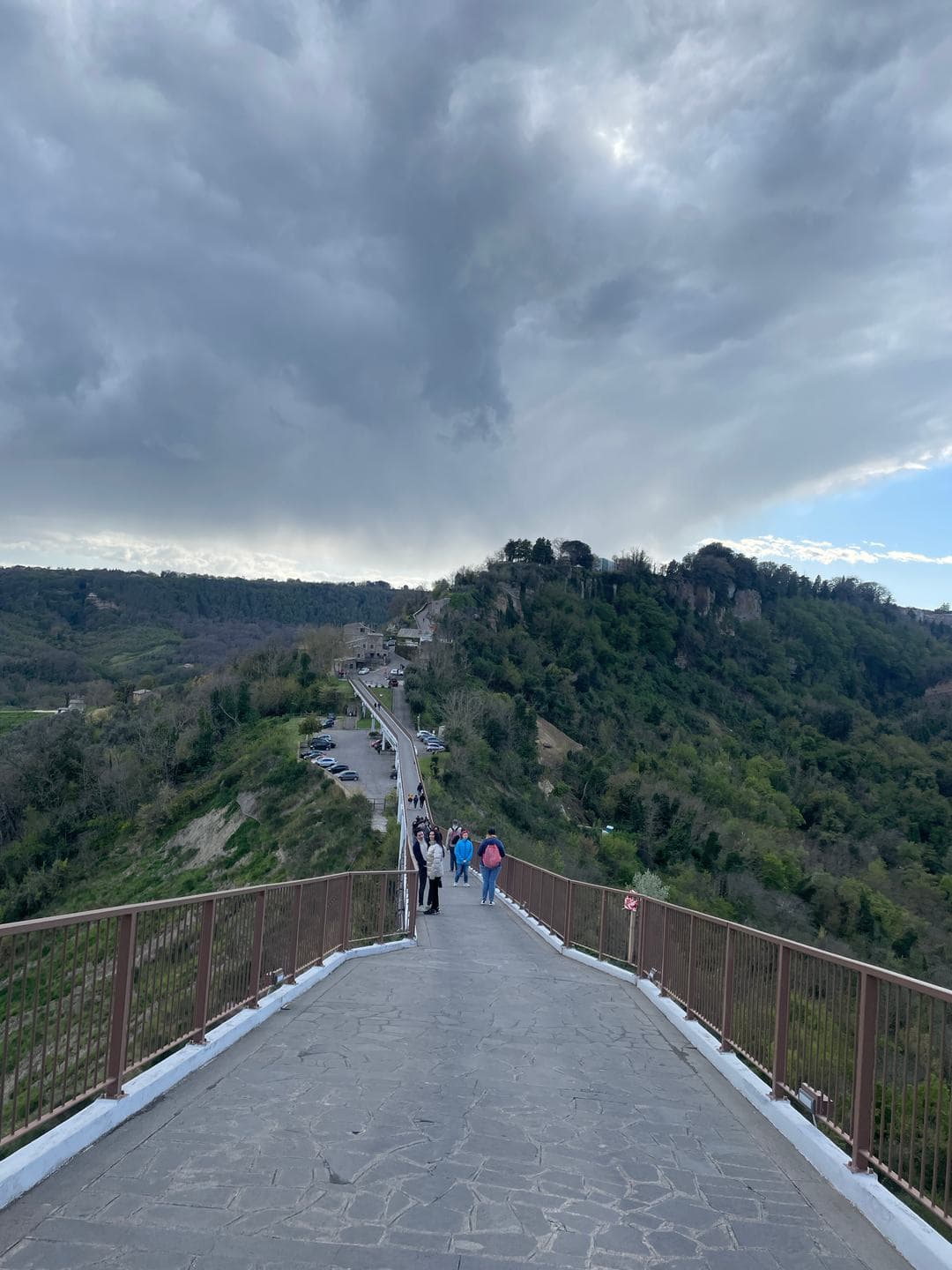 The long pedestrian bridge rising toward the town under heavy clouds