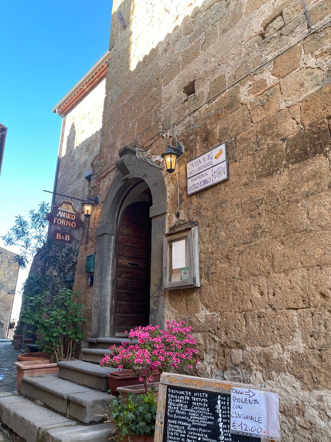 A stone doorway with pink flowers and a chalkboard menu
