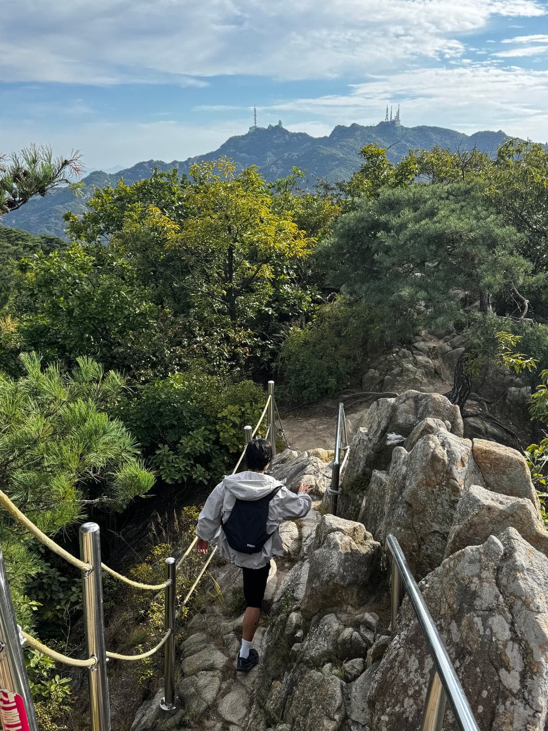 Climbing a rocky section with rope rails toward an antenna-topped peak