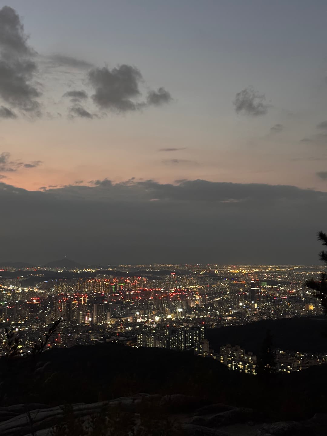 A band of pink sky over the glittering city, seen past the summit rocks