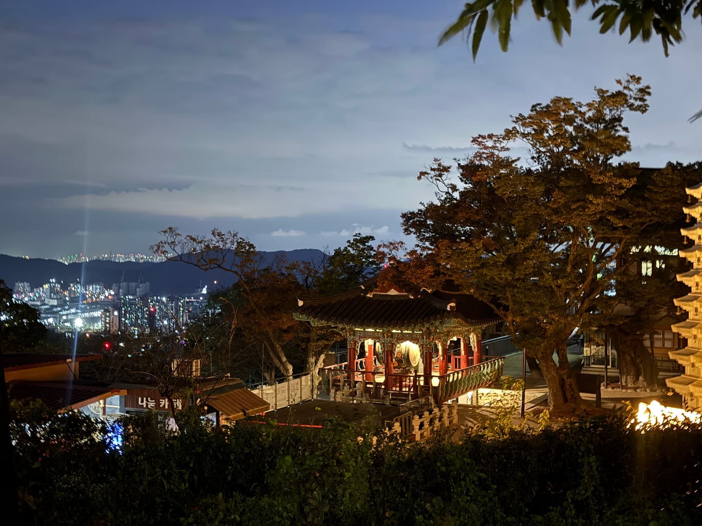 A lit pavilion at the temple with the city lights behind it