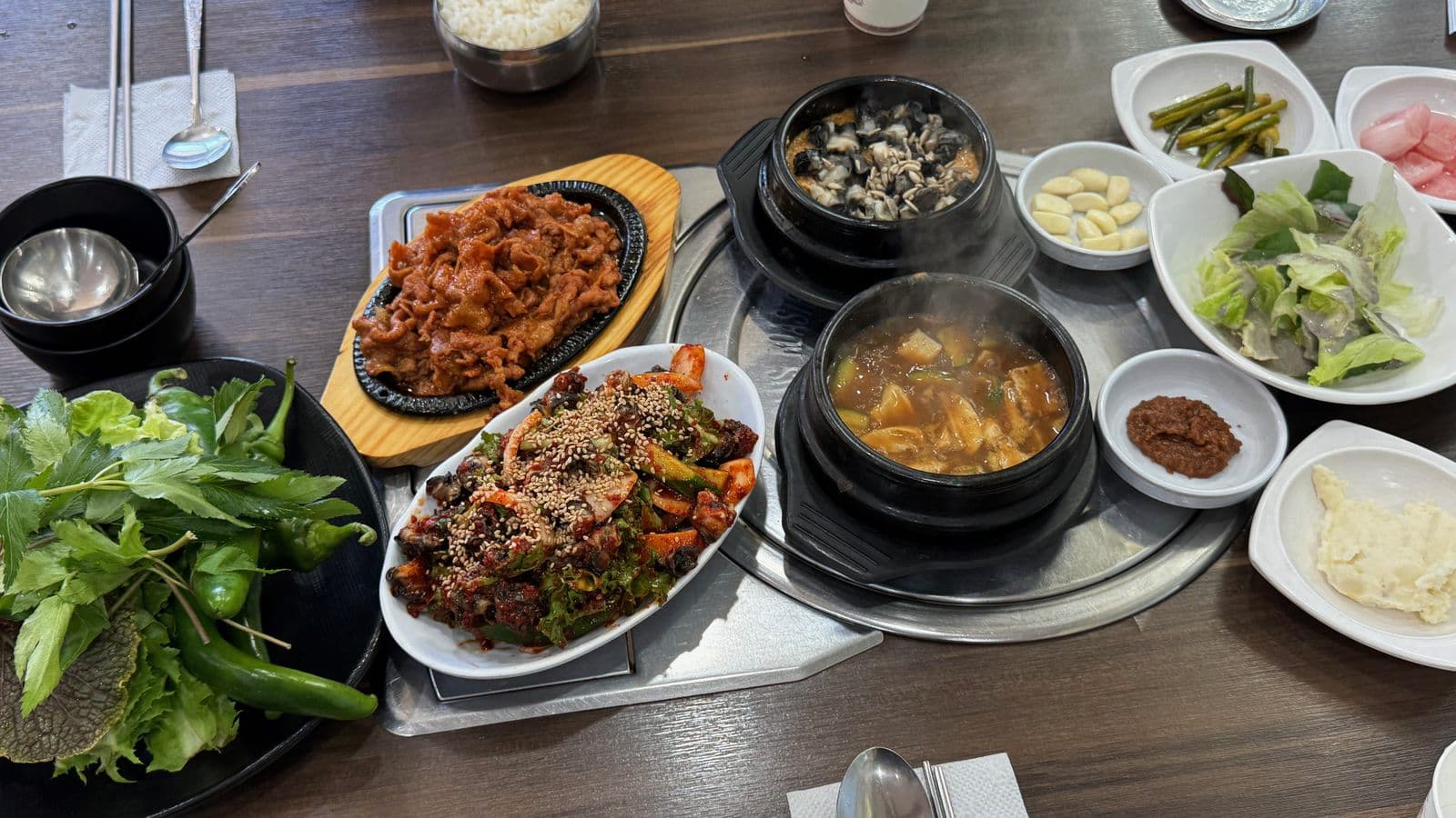 쌈 채소, 철판 제육볶음, 불고기, 우렁 강된장과 된장찌개 뚝배기가 차려진 우렁쌈밥 한 상