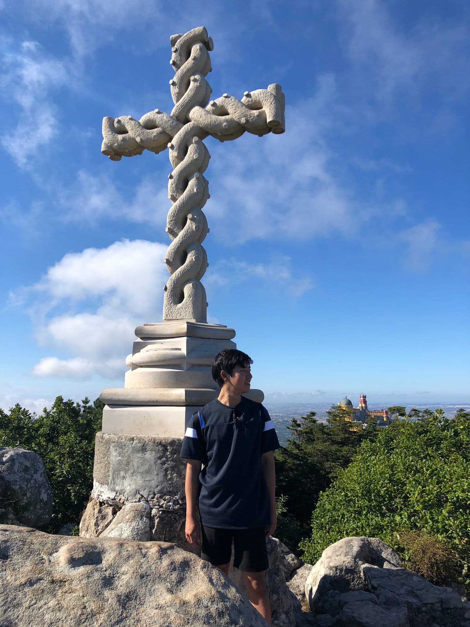 Standing under the stone cross of Cruz Alta, Pena Palace on the hill behind