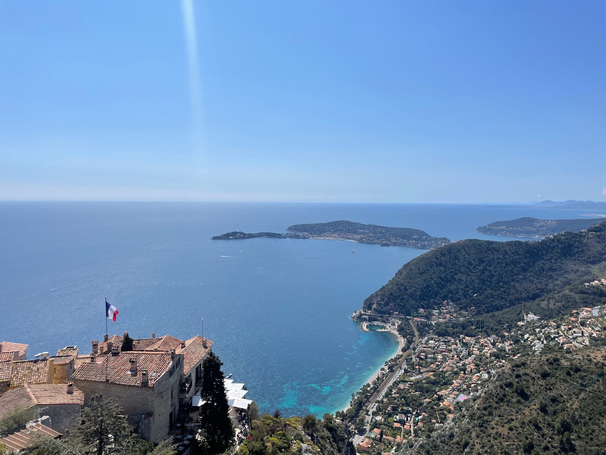 Cap Ferrat and the bay seen from the top of Èze, a French flag over terracotta roofs