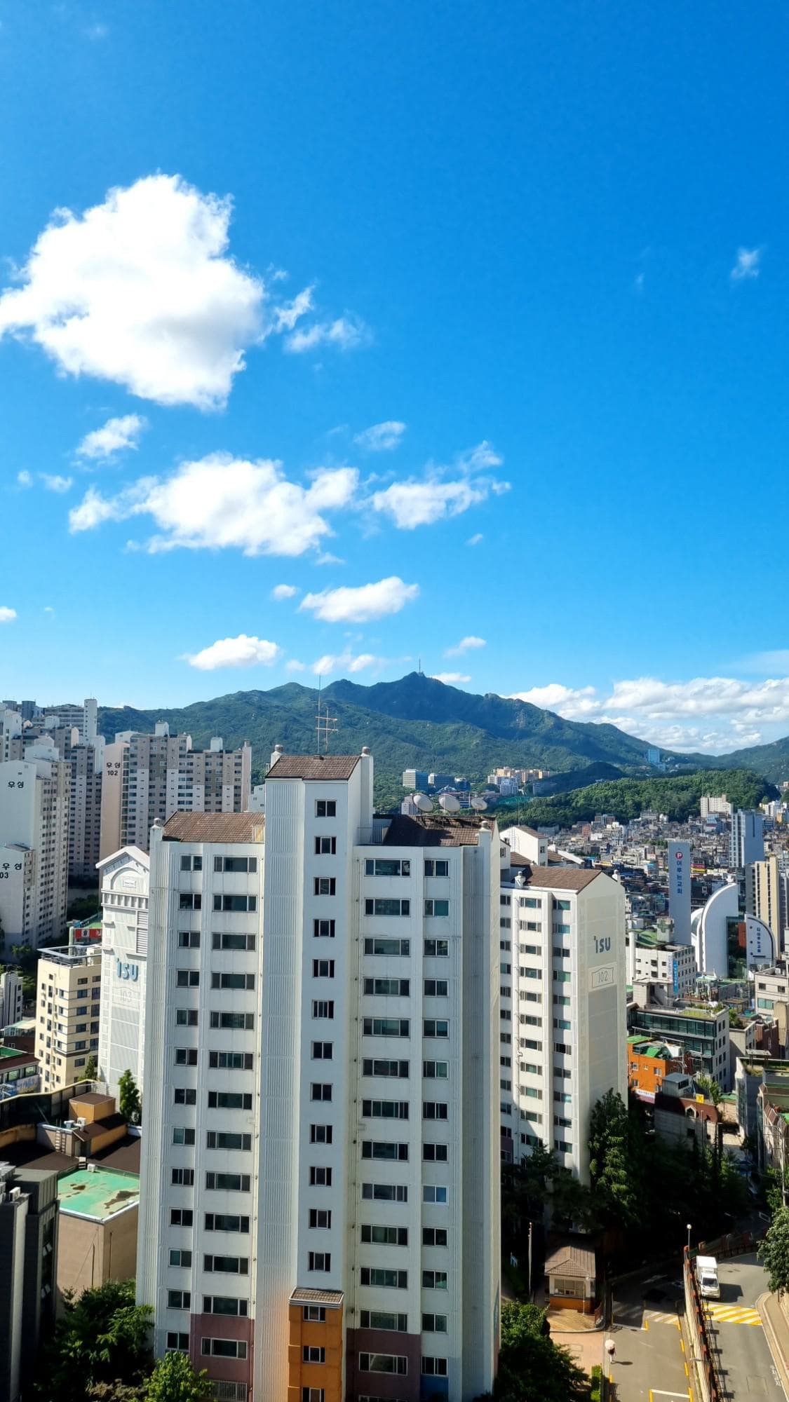 Gwanaksan’s green ridge and summit antenna over white apartment towers under a deep blue sky