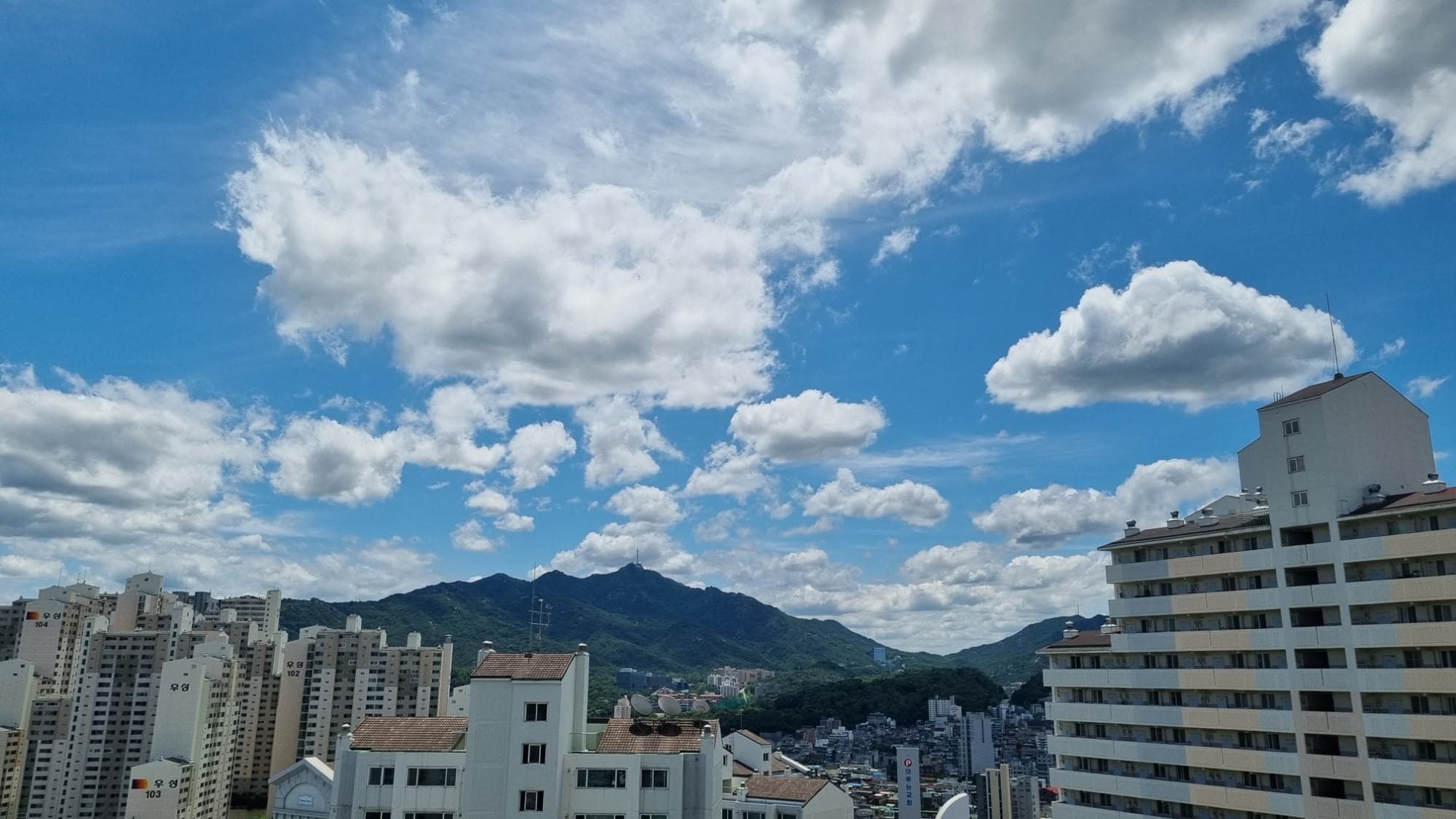 Gwanaksan under big summer clouds, framed by apartment blocks