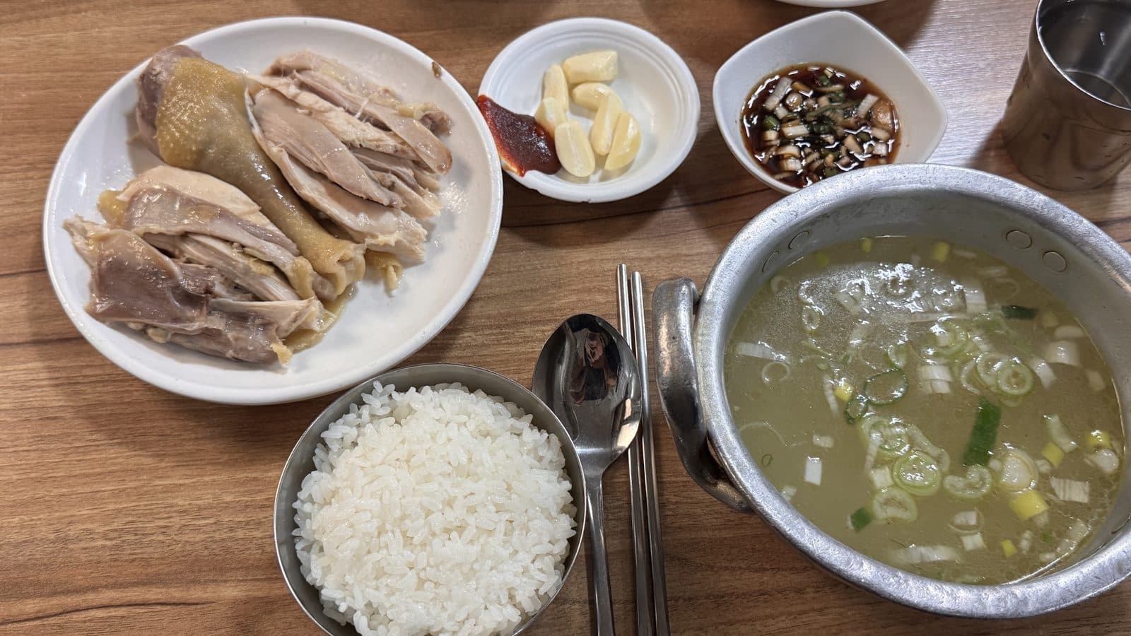 양은 냄비에 담긴 맑은 닭곰탕과 공깃밥, 접시에 따로 나온 닭고기, 김치와 깍두기가 차려진 한 상