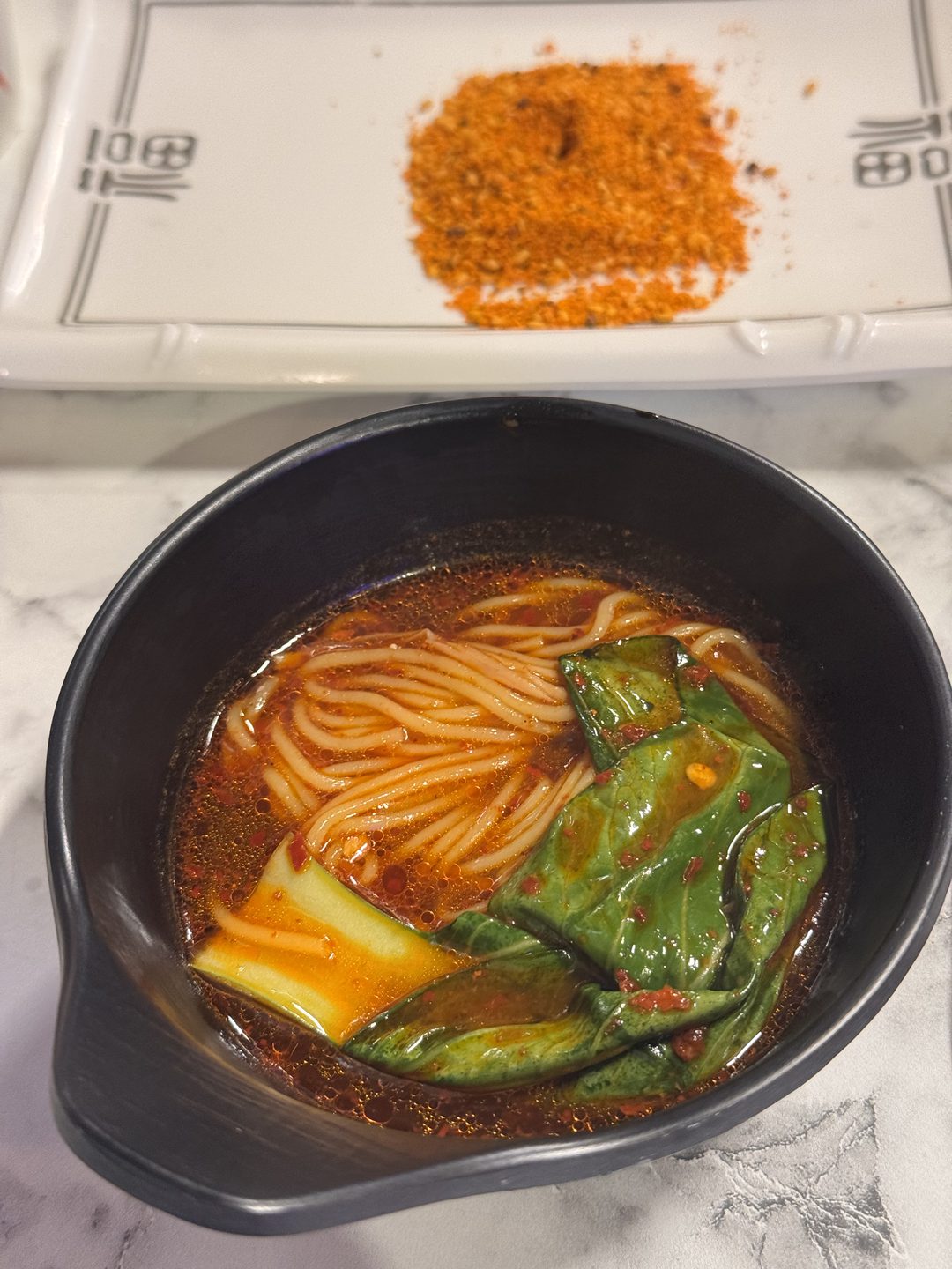 붉은 국물에 면과 청경채가 담긴 온면 한 그릇, 옆에 쯔란 양념 접시