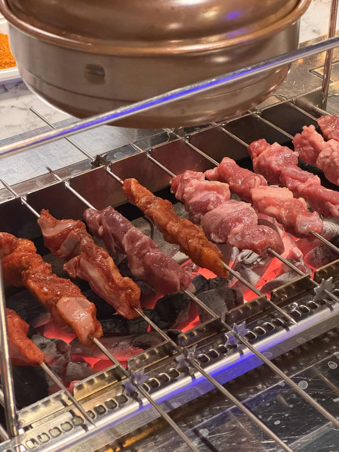 숯불 위 자동 회전 그릴에서 익어 가는 양꼬치와 양념 꼬치