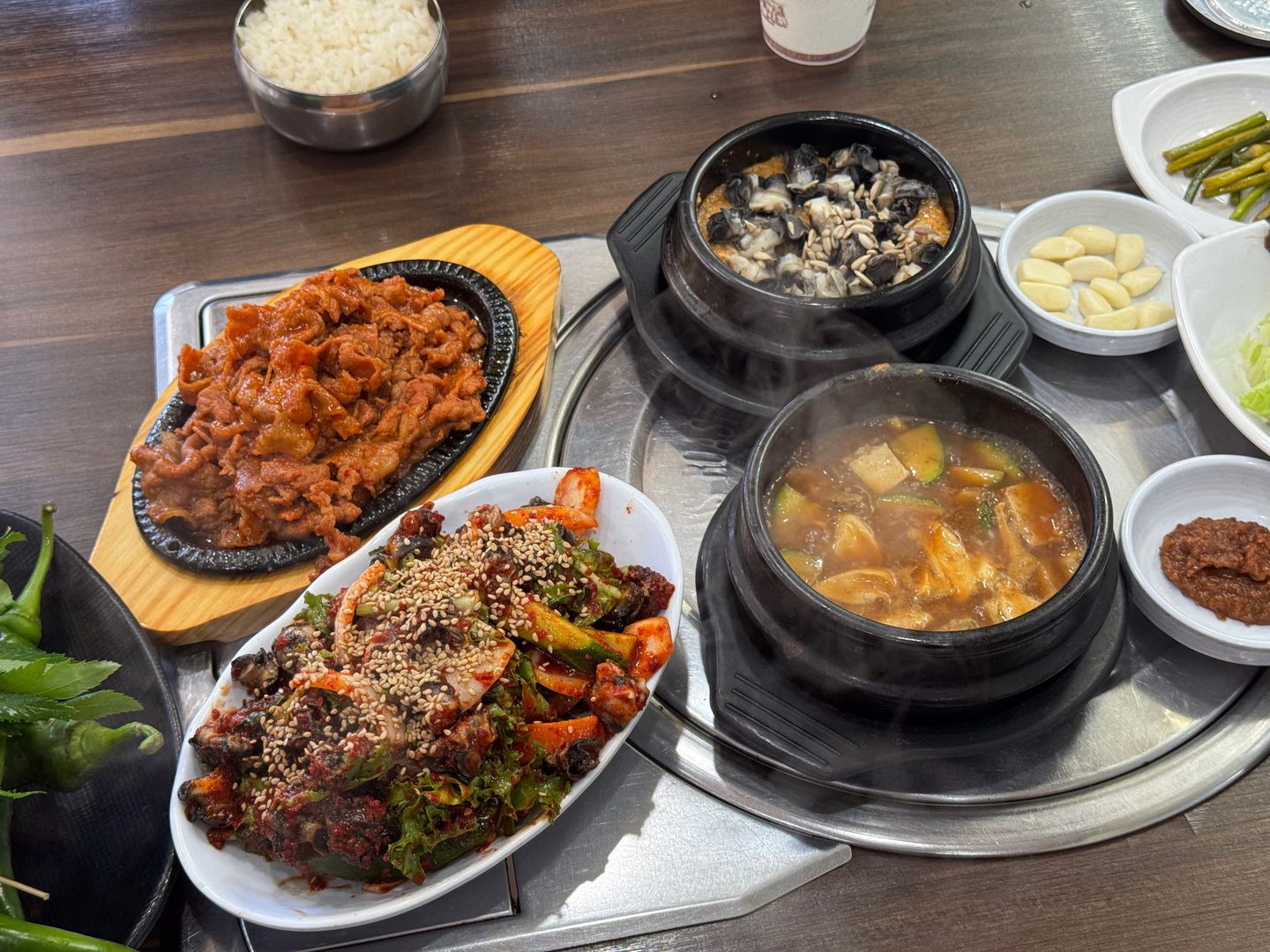 철판 위 빨간 제육볶음과 깨를 뿌린 불고기, 두 개의 뚝배기와 반찬이 놓인 테이블