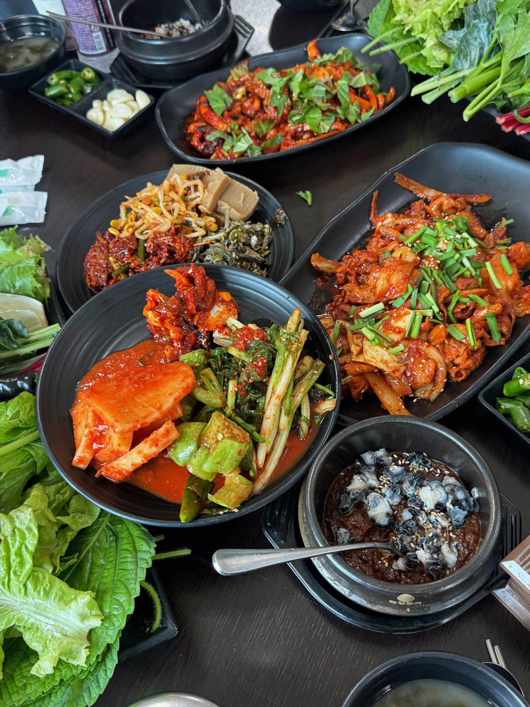김치, 나물, 풋고추 반찬과 쭈꾸미볶음, 우렁 강된장이 함께 놓인 테이블