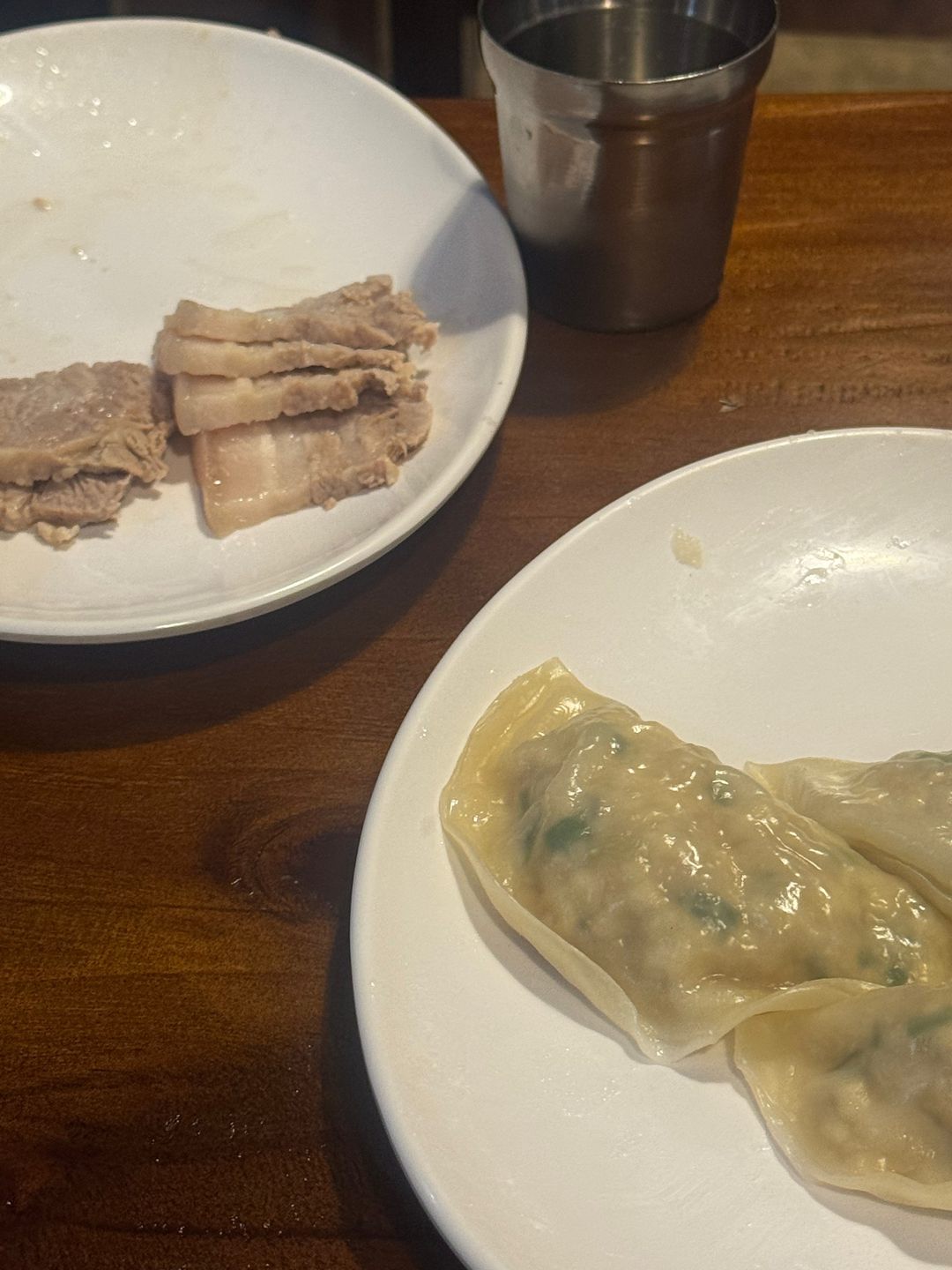 흰 접시에 담긴 얇게 썬 수육과 큼직한 평양만두 두 개