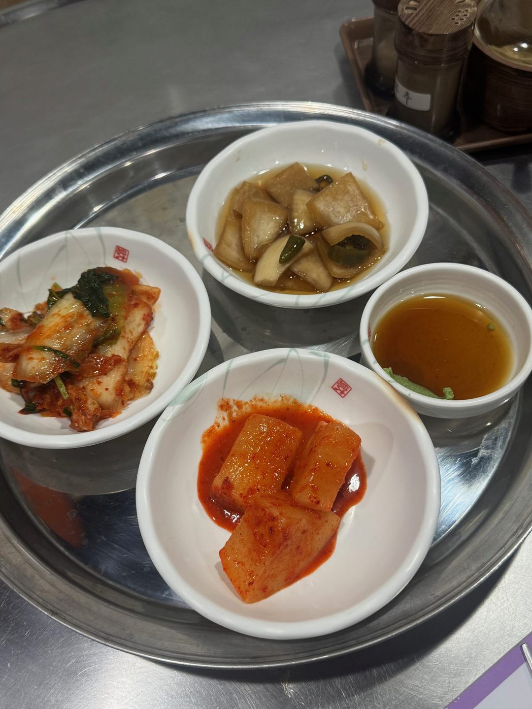 스테인리스 쟁반 위의 깍두기, 배추김치, 간장 장아찌, 간장 소스