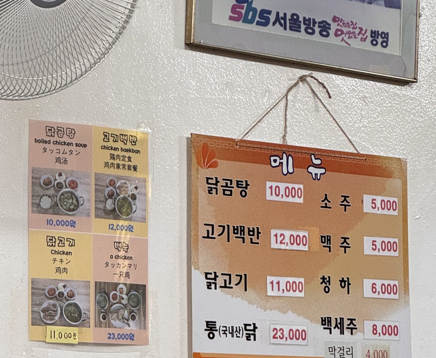 벽에 걸린 메뉴판과 영어·일본어·중국어가 함께 적힌 메뉴 사진, 위에는 SBS 방송 출연 액자가 걸려 있다