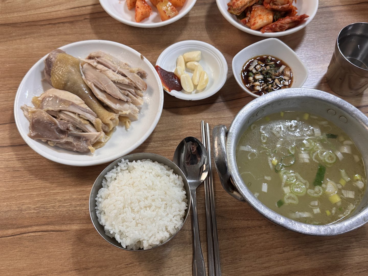 닭곰탕 냄비, 공깃밥, 접시에 담긴 닭고기, 김치와 깍두기, 양념간장과 마늘이 차려진 테이블