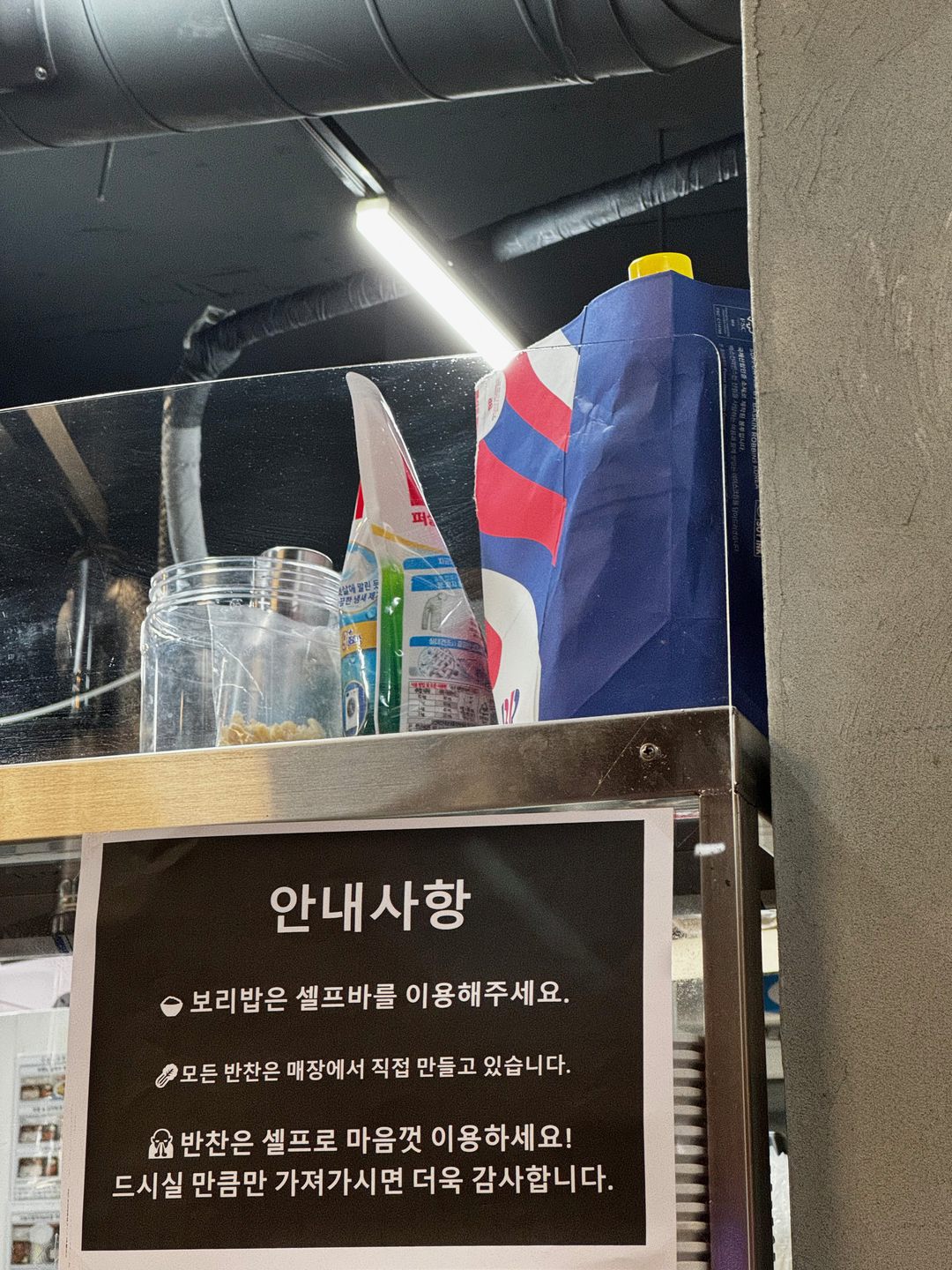 Cartel que dice 'Para el arroz de cebada, usa la barra de autoservicio. Todos los banchan se preparan en el local'